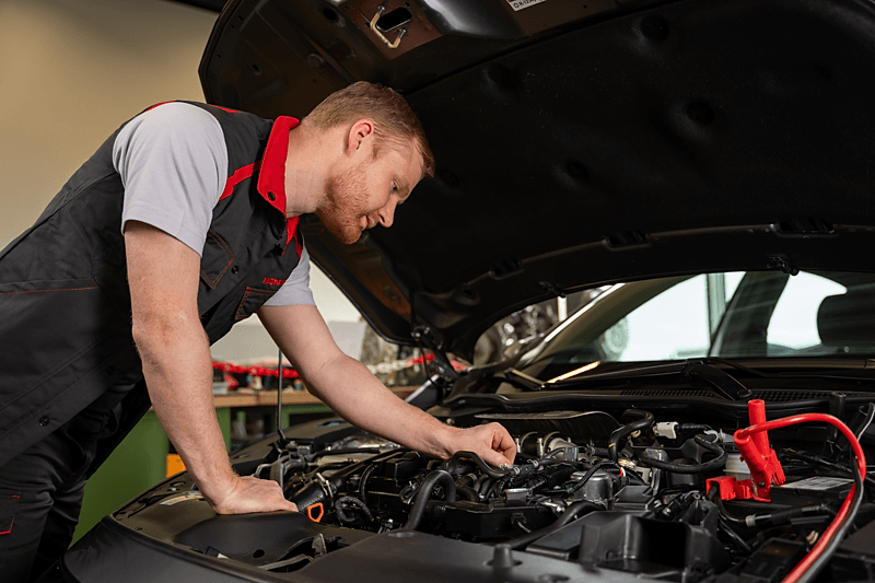 A male leaning on the engine of a Honda car tweaking something in the engine. 